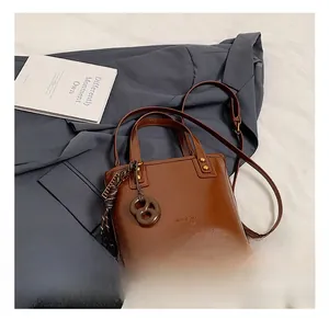 Détail d'un sac seau en similicuir marron avec poignées posé sur un trench-coat classique
