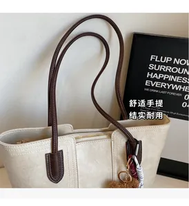 Close-up of the zipper closure, brown straps and decorative charm on white tote bag
