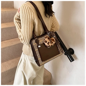 Detail shot of a contrast color tote bag with plaid stitching and a plush leopard heart charm