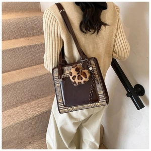 Detail of a brown patchwork tote bag with plaid side panels and a leopard heart charm