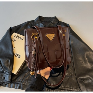 Detalle de bolso tote en charol marrón oscuro con textura trenzada y colgante dorado