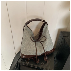 Detail of grey denim and brown leather tote bag with bow accent on a book