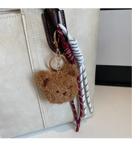 Brown plush bear charm with gold keychain and red braided rope on a cream tote bag