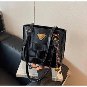Detalle del bolso de hombro trenzado negro con logotipo metálico dorado y adorno de cuerda