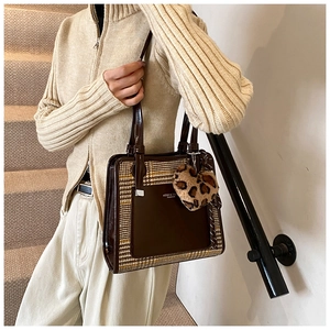Detail of a brown plaid tote bag featuring a plush leopard heart charm on a staircase