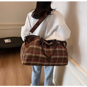 Détail du sac de voyage à carreaux avec poignées en cuir marron et bandoulière réglable