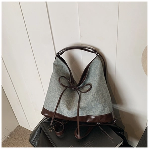 Close-up of denim tote bag with brown leather handles and decorative bow detail