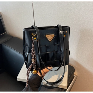 Detalle de bolso tote negro trenzado con placa de logo dorada y colgante de cascabel