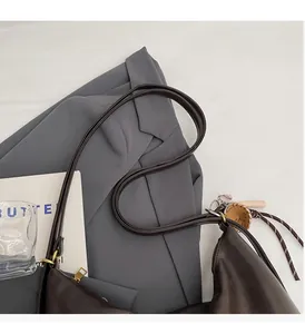 Detail of dark coffee leather half-moon tote bag with baseball glove pendant on gray blazer