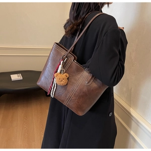 Detail of vintage brown tote bag with white contrast stitching and plush bear charm