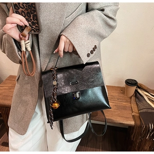 Sac à main noir chic avec rabat scintillant et charm clochette sur un banc en bois