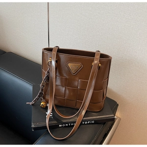 Detalle del bolso tote marrón trenzado con logo metálico y colgante de campana