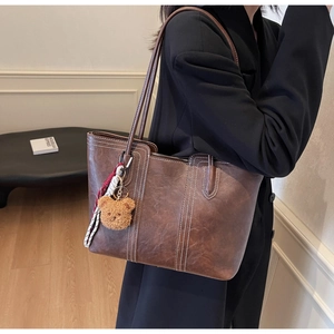 Detail of dark brown tote bag with contrast stitching and plush bear charm accessory