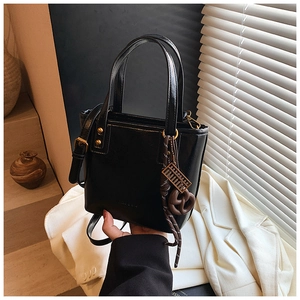 Détail d'un sac seau en cuir noir avec rivets dorés et pendentif de boulier