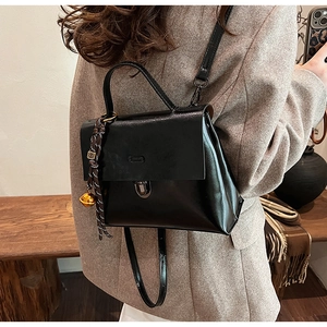 Detailansicht schwarze glänzende Handtasche mit goldenem Glockenanhänger und Riemen