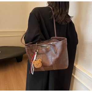 Detail view of large brown leather tote bag with white contrast stitching and bear charm