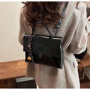 Détail d'un sac bandoulière noir brillant avec boucle métallique et breloque tressée