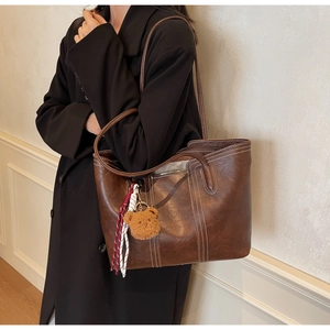 Close-up of a large dark brown leather tote bag with white contrast stitching and charm