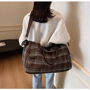 Détail d'un grand sac de voyage à carreaux marron montrant le tissu et les anses en cuir