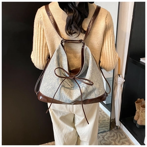 Detail showing blue denim texture with brown leather straps and bow on the backpack
