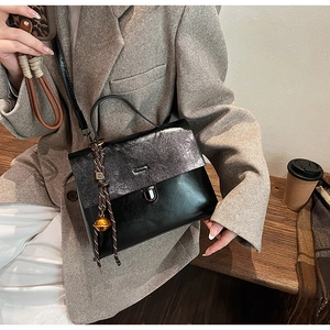 Detail einer eleganten zweifarbigen Handtasche mit glitzernder Klappe und Glockenanhänger