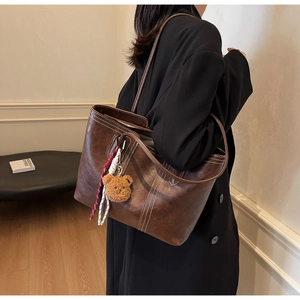 Detail of vintage brown tote bag with contrast stitching and plush bear charm