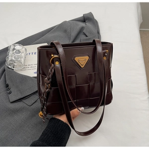 Detalle de bolso shopper trenzado marrón oscuro con logo metálico y nudo decorativo