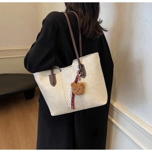 Close-up of cream tote bag with brown straps and a cute plush bear charm detail