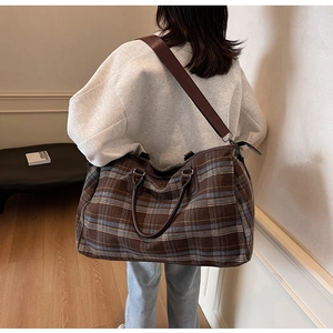 Détail d'un grand sac de voyage à carreaux marron et bleu avec anses en cuir sur un modèle
