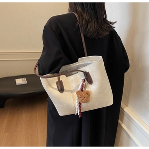 Detail of cream tote bag with brown straps and cute teddy bear charm accessory