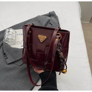 Primer plano de bolso tote trenzado burdeos con logo dorado sobre un blazer gris