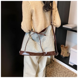 Detail of a large light blue denim tote bag with brown leather straps worn over the shoulder