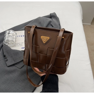 Detalle del bolso tote de piel trenzada marrón oscuro con placa de logo metálica dorada