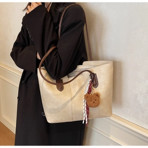 Detailed view of large beige tote bag with brown straps and plush bear keychain decoration