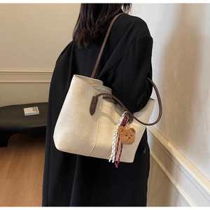 Close-up of minimalist beige tote bag with dark brown straps and plush bear charm
