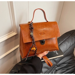 Détail d'un sac à main en cuir marron texturé avec fermoir métallique et breloque