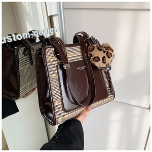 Detail of a brown tote bag with houndstooth stitching and a leopard heart charm