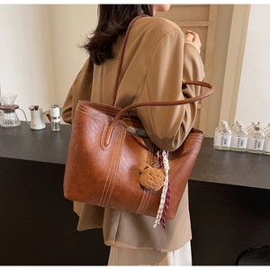 Detail of a large brown faux leather tote bag with white stitching and bear charm