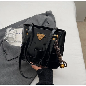 Detalle del bolso tote trenzado en charol negro brillante con placa de metal