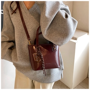 Détail du sac seau en cuir bordeaux avec pendentif tressé et logo embossé