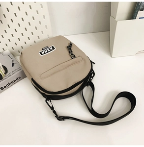 Détail du sac bandoulière en toile beige avec étiquette de mode noire et bandoulière
