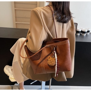 Detail of a brown leather tote bag with white stitching and plush bear charm decoration