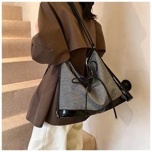 Side view of large grey tote bag with black leather trim worn by model on shoulder