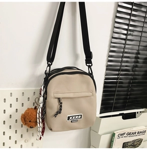 Détail de la sacoche en nylon beige avec poche zippée et breloque ours en peluche