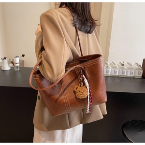 Close-up of large dark brown leather tote bag with white stitching and bear charm