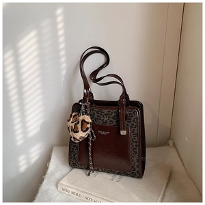 Detail of a brown patent leather tote bag with leopard print trim and a heart-shaped charm
