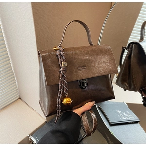 Détail d'un sac à main vintage en cuir marron avec fermoir métallique et breloque tissée