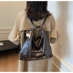 Detail of a dark brown PU leather tote backpack with metal buckles and baseball charm