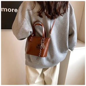 Détail du sac seau en cuir ciré marron vintage avec breloque tressée et logo rond