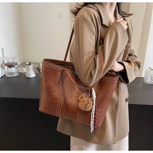 Detail of vintage brown leather tote bag with white stitching and plush bear charm